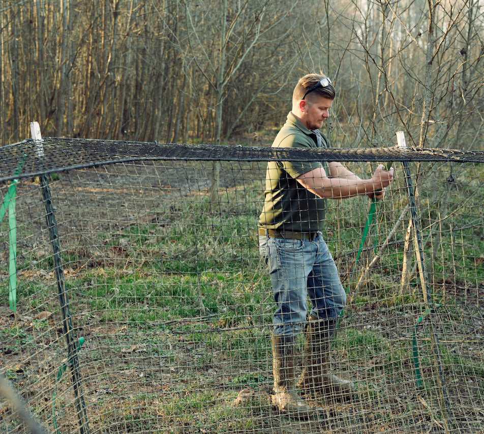 Man working on a trap in a field with trees in the background