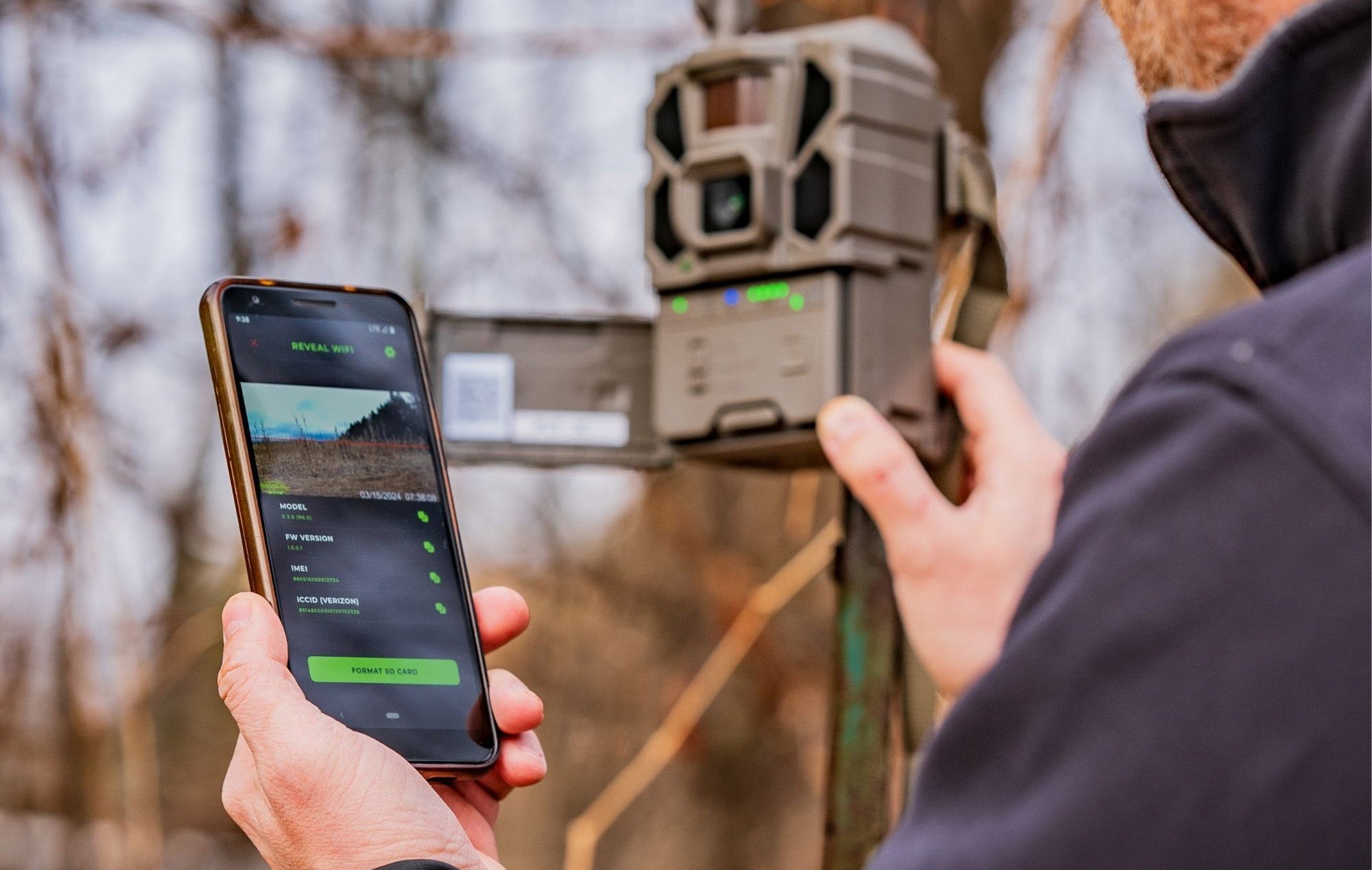 Person using a smartphone app with a wildlife camera in a natural setting