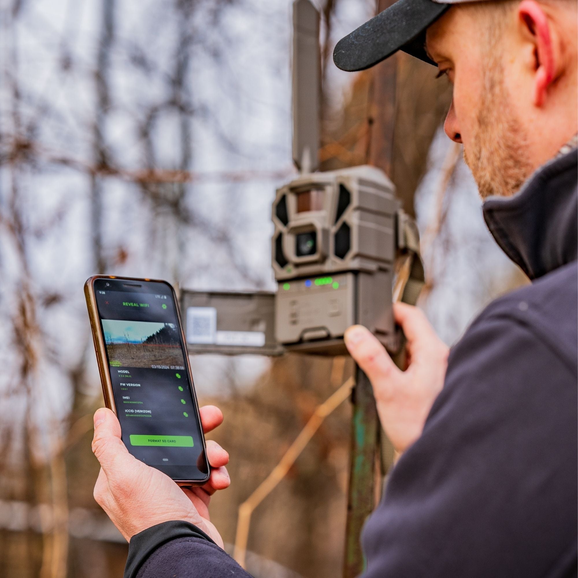 Man using a smartphone to control a hunting camera trap in a forest setting